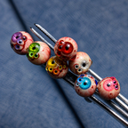 Seven colorful Thousandfold Omen multi-eye tops arranged in tweezers